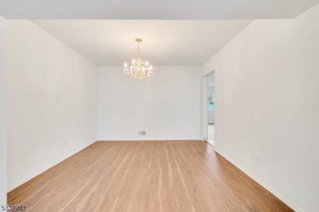 empty room with light hardwood / wood-style floors and a notable chandelier