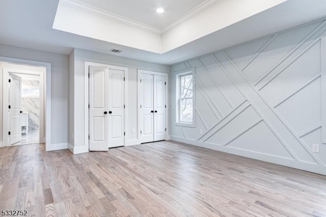 unfurnished bedroom with ensuite bath, two closets, ornamental molding, and light hardwood / wood-style floors