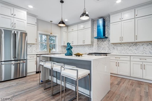 kitchen with appliances with stainless steel finishes, a kitchen breakfast bar, white cabinetry, and wall chimney exhaust hood