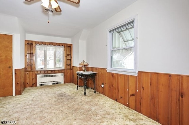 interior space featuring ceiling fan, radiator heating unit, wood walls, and carpet flooring