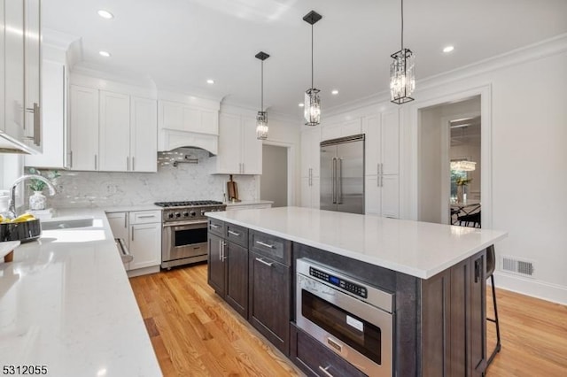 kitchen featuring light wood-type flooring, sink, built in appliances, a center island, and white cabinetry