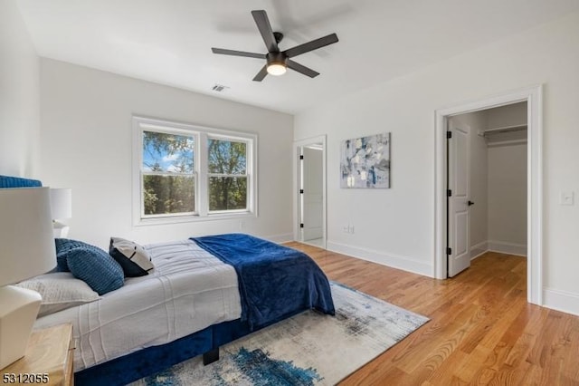 bedroom featuring ceiling fan, a closet, a walk in closet, and light hardwood / wood-style flooring