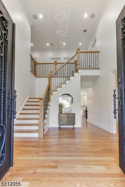 foyer entrance featuring wood-type flooring, crown molding, and a notable chandelier