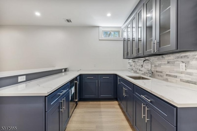 kitchen with sink, decorative backsplash, light wood-type flooring, light stone counters, and kitchen peninsula