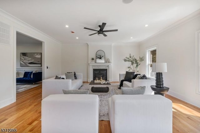 living room with light wood-type flooring, ceiling fan, ornamental molding, and a premium fireplace