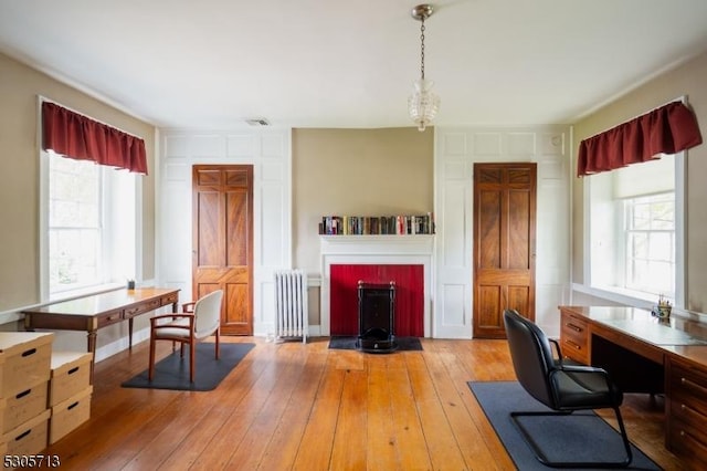 home office featuring light hardwood / wood-style floors, radiator heating unit, and an inviting chandelier