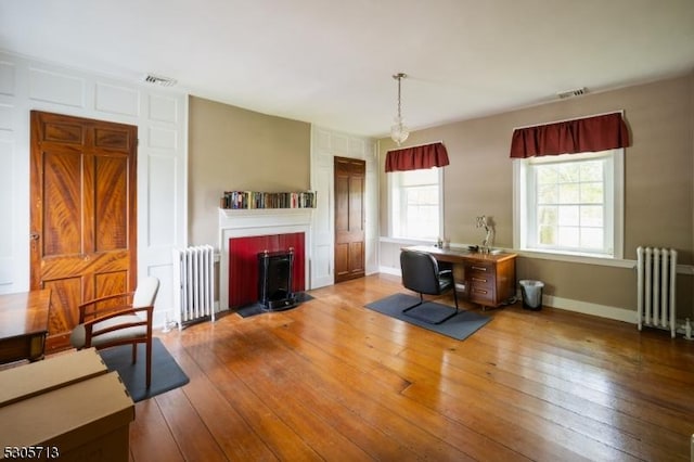 dining space featuring a brick fireplace, wood-type flooring, and radiator heating unit