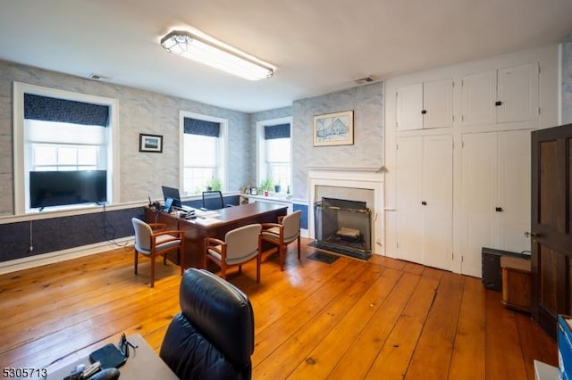 office with light hardwood / wood-style floors and a large fireplace