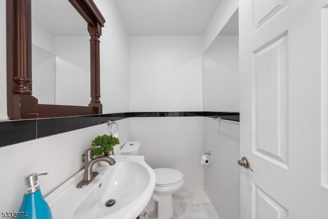 bathroom featuring toilet, tile walls, and sink