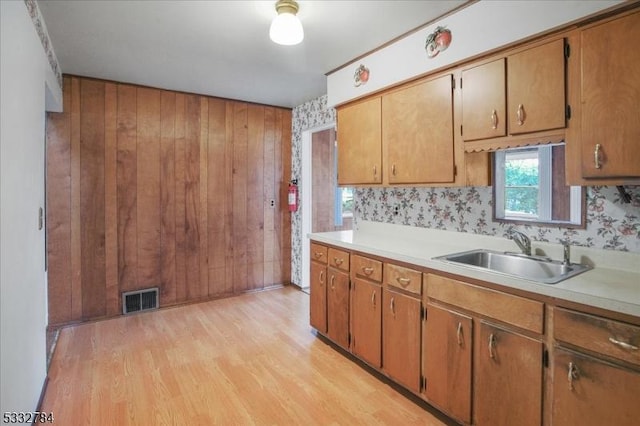 kitchen featuring wooden walls, sink, and light wood-type flooring