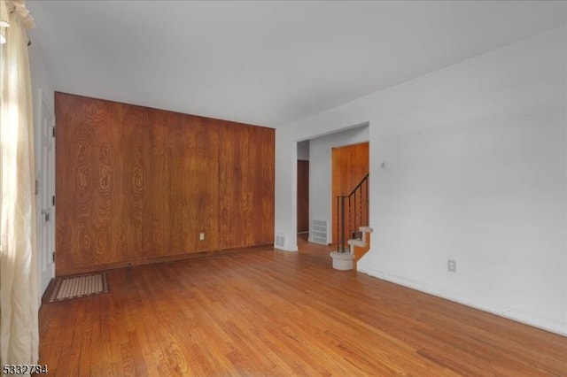 unfurnished room featuring light wood-type flooring and wooden walls