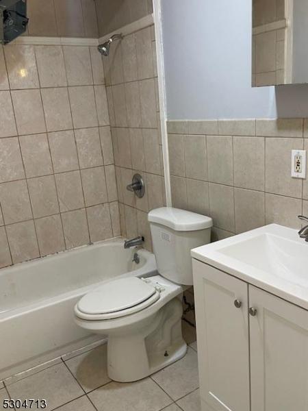 full bathroom featuring tiled shower / bath combo, tile patterned floors, toilet, vanity, and tile walls