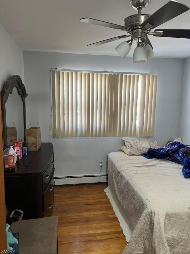 bedroom featuring ceiling fan, hardwood / wood-style flooring, multiple windows, and a baseboard radiator