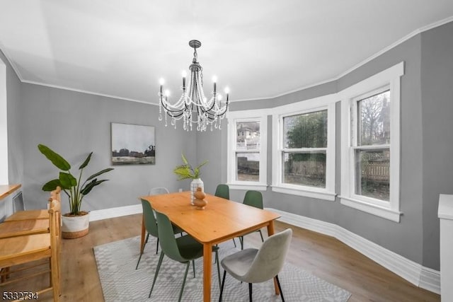 dining area with hardwood / wood-style flooring, crown molding, and an inviting chandelier