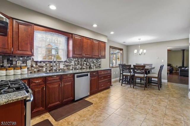 kitchen featuring decorative light fixtures, a notable chandelier, appliances with stainless steel finishes, dark stone countertops, and sink