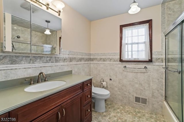 full bathroom featuring tile walls, toilet, vanity, and shower / bath combination with glass door