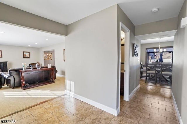 hallway featuring light colored carpet and an inviting chandelier