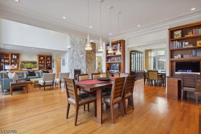 dining area featuring ornamental molding, light hardwood / wood-style flooring, a stone fireplace, and built in shelves