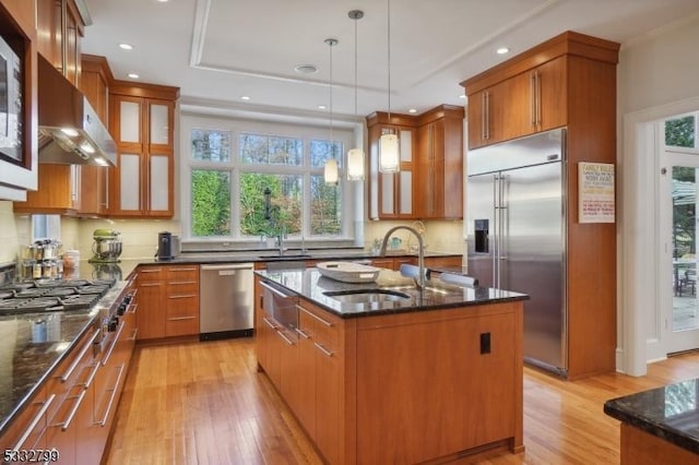 kitchen featuring extractor fan, pendant lighting, a center island with sink, appliances with stainless steel finishes, and sink