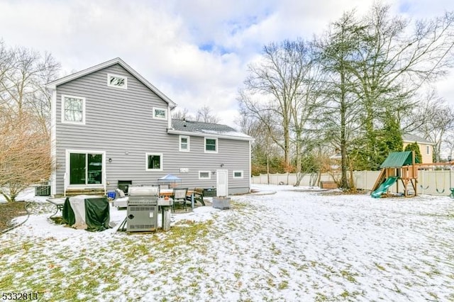 snow covered back of property with a playground