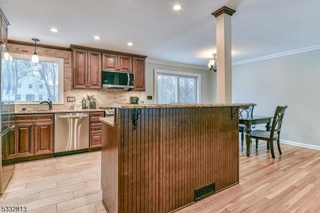 kitchen with stainless steel appliances, light hardwood / wood-style flooring, decorative light fixtures, and a kitchen breakfast bar