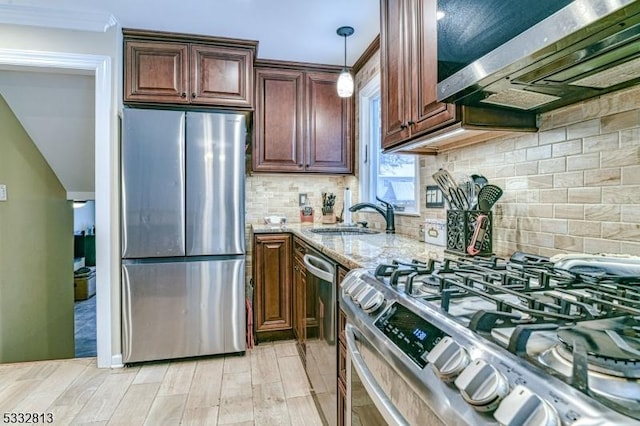 kitchen featuring appliances with stainless steel finishes, light wood-type flooring, light stone countertops, pendant lighting, and sink