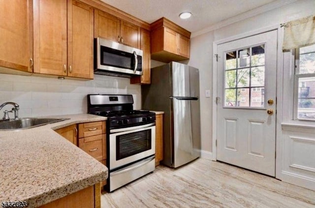 kitchen featuring sink, stainless steel appliances, light stone counters, backsplash, and crown molding