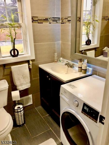 bathroom featuring vanity, tile patterned floors, toilet, tile walls, and washer / dryer