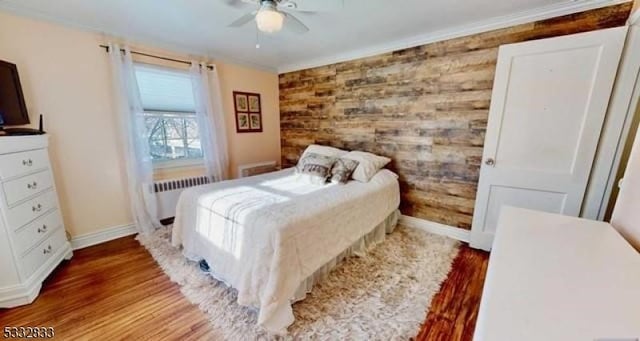 bedroom featuring ornamental molding, ceiling fan, wooden walls, wood-type flooring, and radiator heating unit