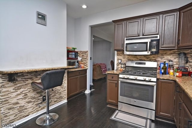 kitchen featuring light stone countertops, appliances with stainless steel finishes, backsplash, and dark brown cabinetry