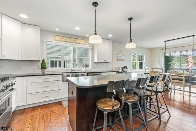 kitchen featuring sink, white cabinets, a center island, stainless steel range, and pendant lighting