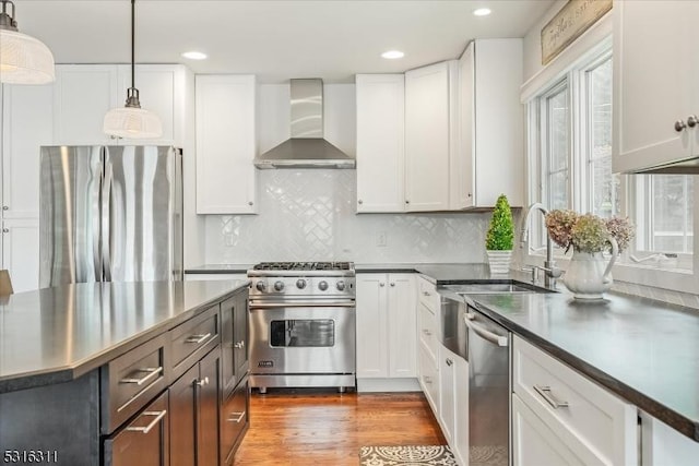 kitchen with stainless steel appliances, wall chimney exhaust hood, white cabinets, and pendant lighting