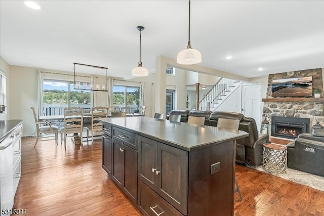 kitchen with decorative light fixtures, a kitchen island, a fireplace, wood-type flooring, and dark brown cabinetry