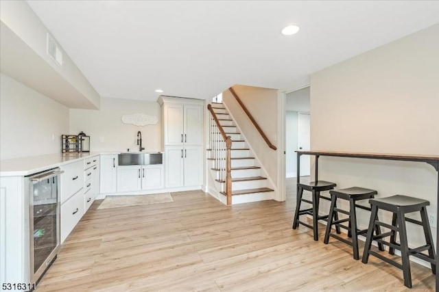 bar with sink, beverage cooler, light hardwood / wood-style floors, and white cabinetry