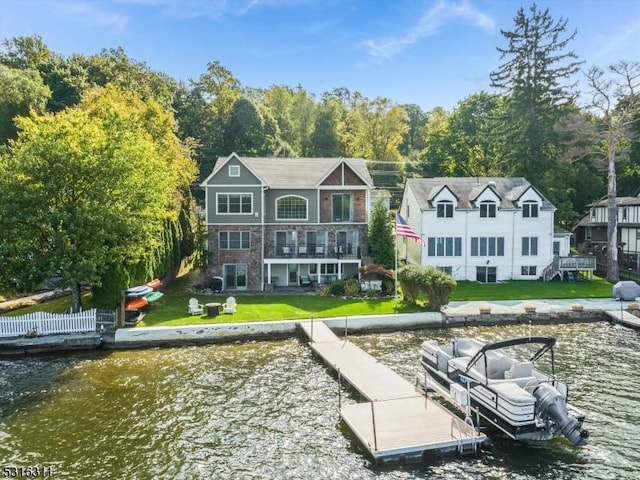 rear view of house featuring a balcony, a water view, and a lawn