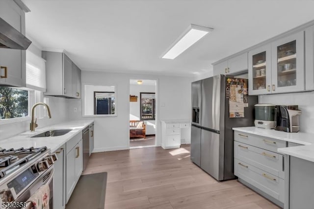 kitchen with appliances with stainless steel finishes, light hardwood / wood-style flooring, a wealth of natural light, and wall chimney exhaust hood