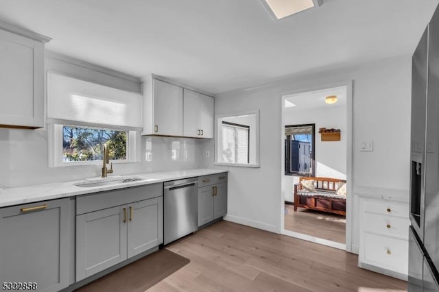 kitchen with sink, gray cabinetry, light wood-type flooring, and stainless steel dishwasher