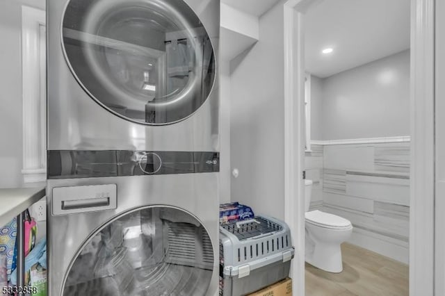 laundry room with stacked washer / drying machine, tile walls, and hardwood / wood-style flooring