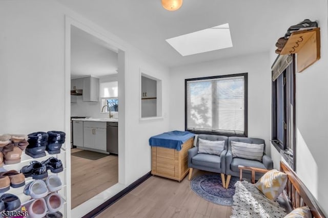 living area with light hardwood / wood-style floors, a skylight, and sink