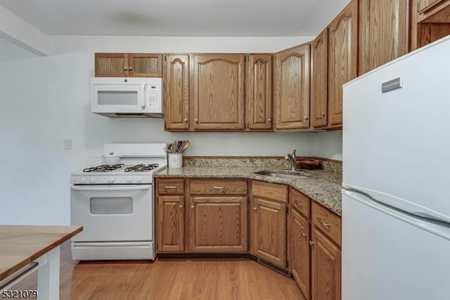 kitchen with white appliances, light hardwood / wood-style floors, light stone counters, and sink