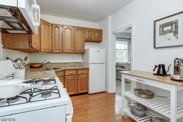 kitchen with sink, white appliances, light hardwood / wood-style floors, and light stone countertops