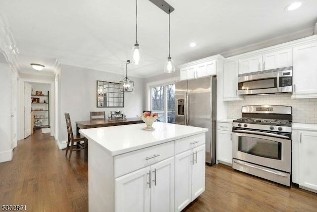 kitchen featuring decorative light fixtures, white cabinets, backsplash, a kitchen island, and appliances with stainless steel finishes