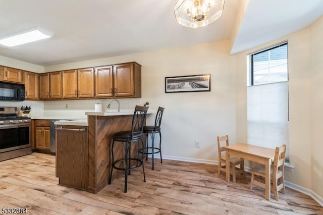 kitchen featuring kitchen peninsula, decorative backsplash, stainless steel range with gas stovetop, light hardwood / wood-style flooring, and a kitchen breakfast bar