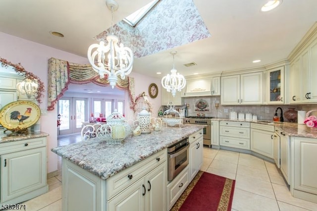 kitchen with hanging light fixtures, light tile patterned floors, a kitchen island, an inviting chandelier, and appliances with stainless steel finishes