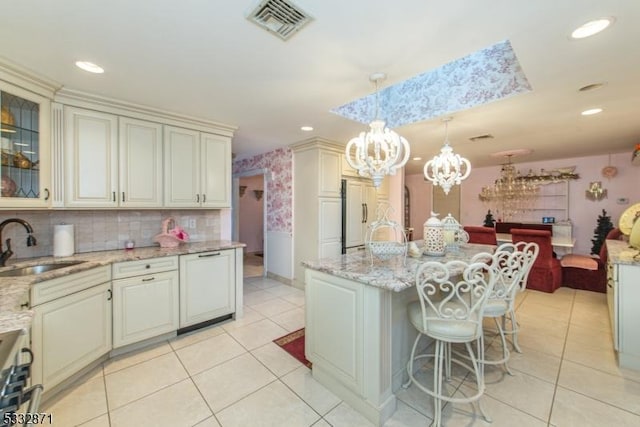 kitchen featuring hanging light fixtures, cream cabinetry, a kitchen island, light tile patterned flooring, and sink