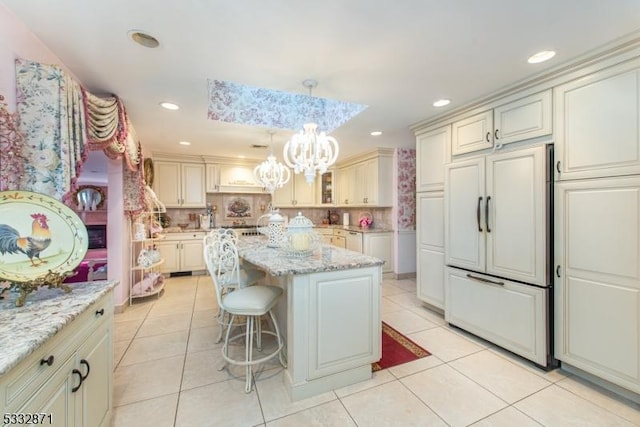 kitchen with paneled fridge, a center island, light tile patterned floors, pendant lighting, and light stone counters