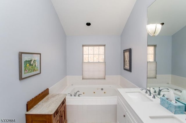 bathroom featuring tiled tub, vaulted ceiling, and vanity