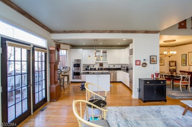 kitchen with stainless steel appliances, white cabinets, light hardwood / wood-style floors, and hanging light fixtures