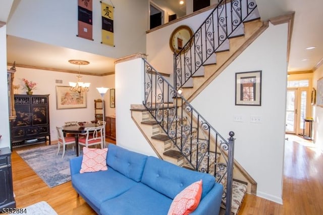 staircase featuring a high ceiling, a notable chandelier, crown molding, and wood-type flooring