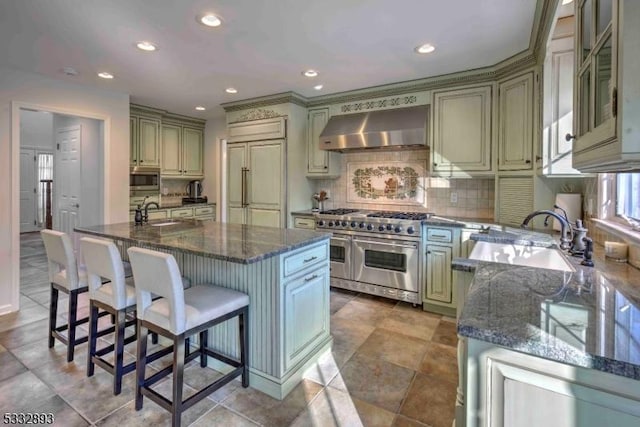 kitchen with tasteful backsplash, wall chimney range hood, a kitchen bar, high end appliances, and a kitchen island with sink